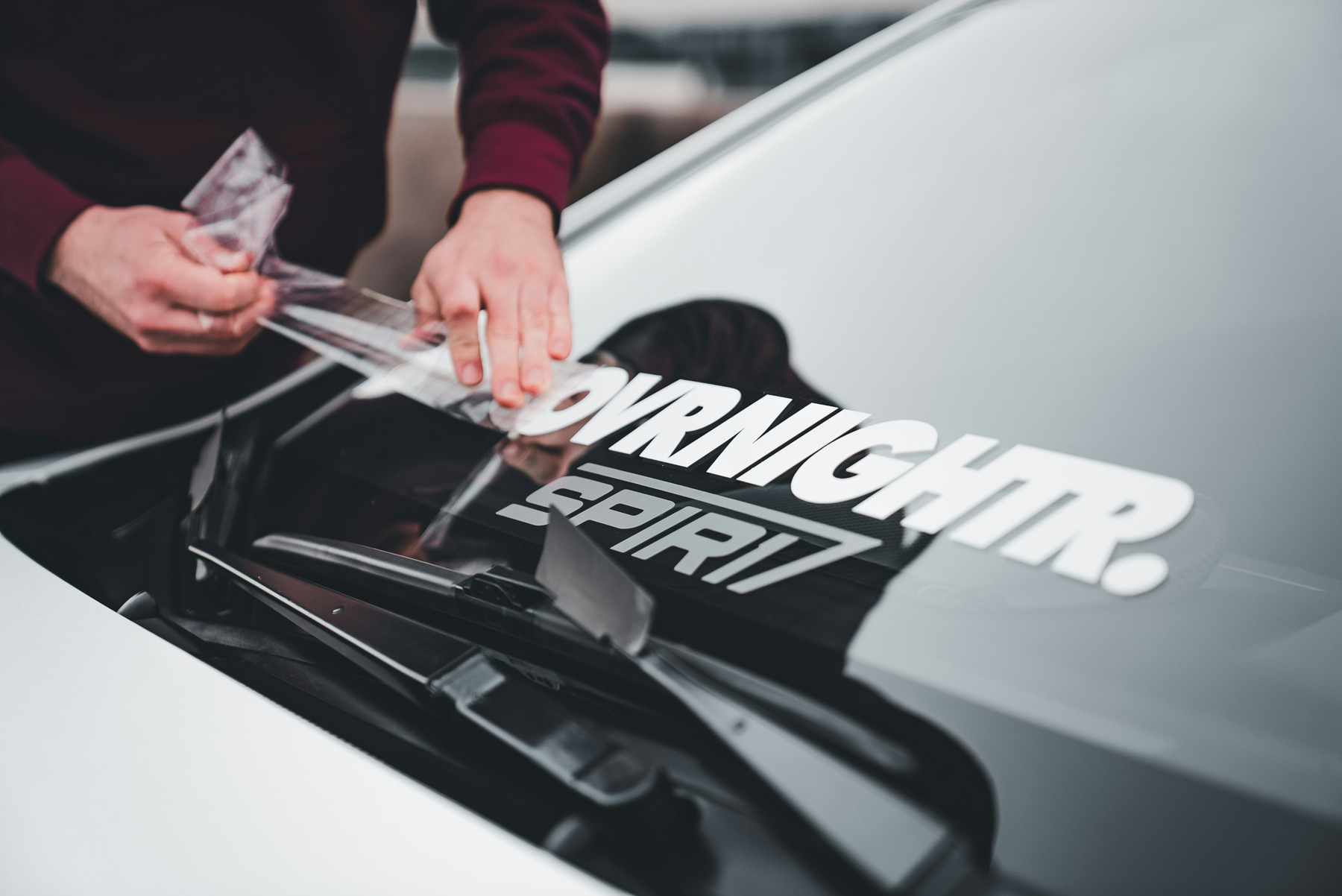 Hand klebt Aufkleber sorgfältig auf eine Autoscheibe